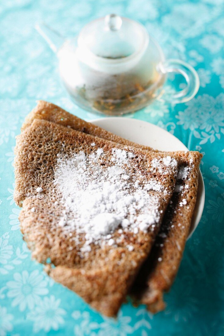 Buckwheat pancake with icing sugar and a teapot