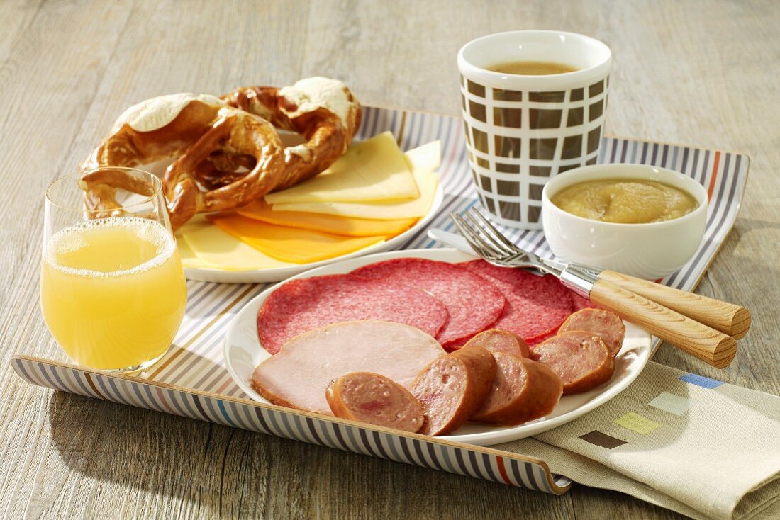 Frühstück auf dem Tablett mit Aufschnitt, Käse, Brezen, Saft, Apfelmus und Tee