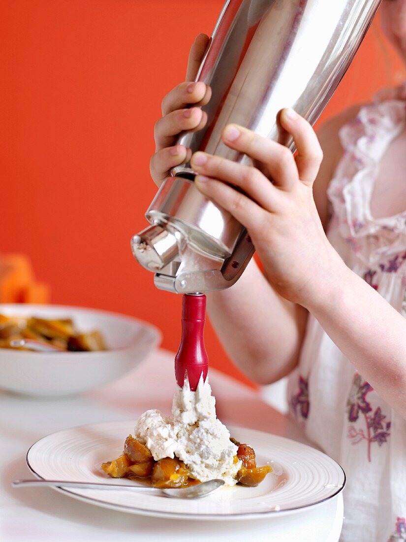 Young girl spraying whipped cream onto stewed mirabelle plums with cinnamon