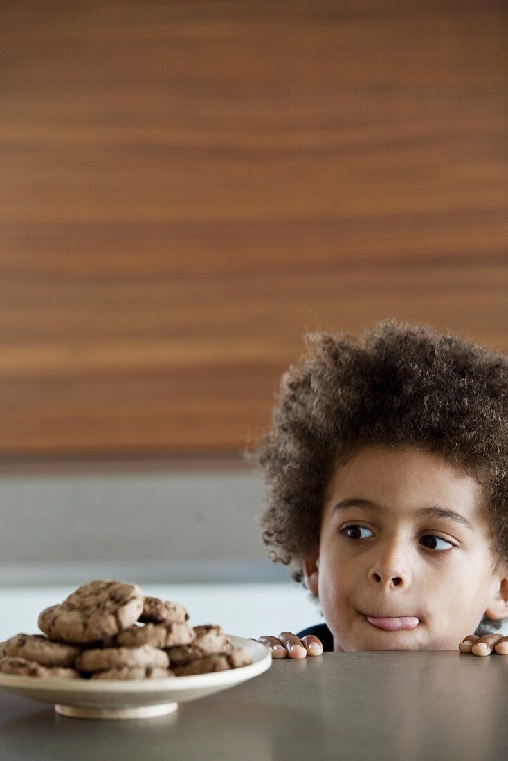 Young boy licking his lips infront of a plate of delicious cookies