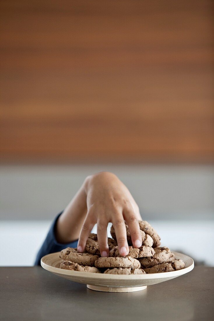 Child's hand stealing a cookie from a plate of cookies