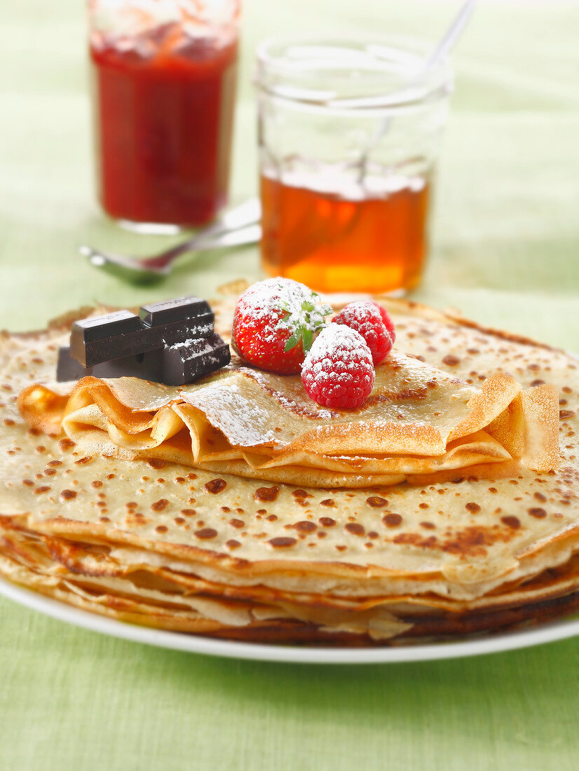 Stacked pancakes with summer fruit,chocolate jars of jam and icing sugar