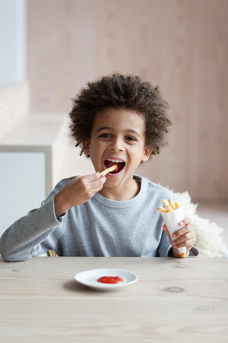 Junge isst eine Tüte Pommes mit Ketchup