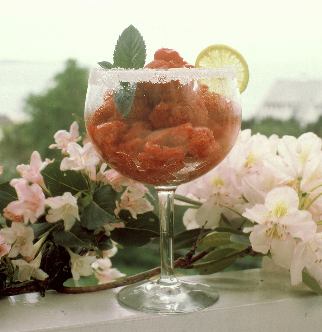 Frozen Strawberry Margarita im Glas vor rosa Blüten