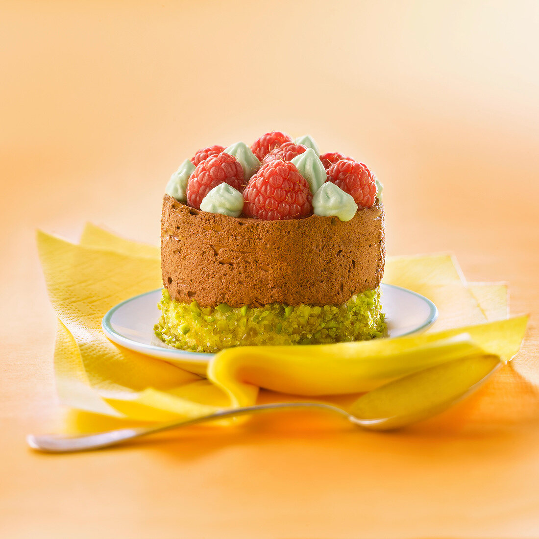 Pistachio and chocolate mousse cake topped with raspberries and pistachio whipped cream