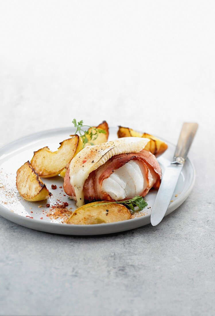 Piece of cod wrapped in bacon and topped with grilled Munster cheese, roast potatoes