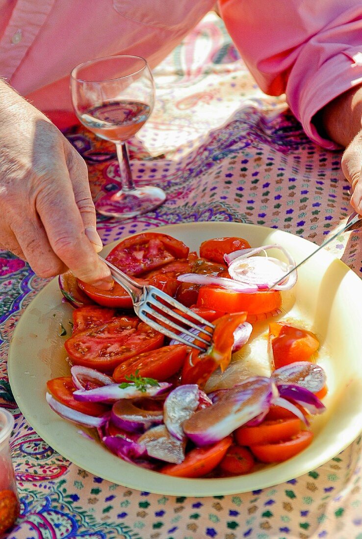 Person durchmischt Tomatensalat mit roten Zwiebeln