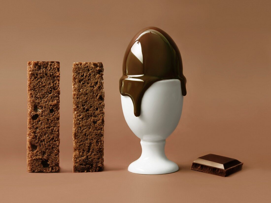 Zwei Streifen Schokoladenkuchen, schmelzendes Ei im Eierbecher und Schokoladenstück
