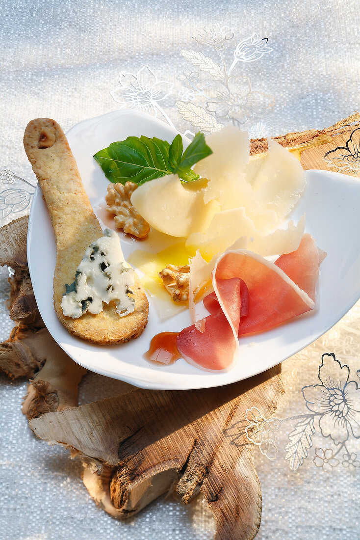 Vorspeisenteller mit Parmesan, Parmaschinken, Walnüssen und Roquefort auf Gebäck in Löffelform