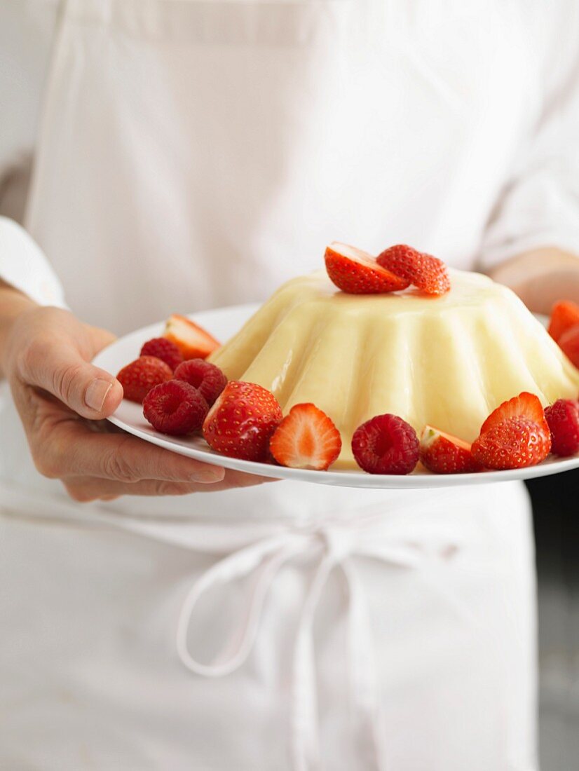 Person hält einen Teller Pudding mit Erdbeeren und Himbeeren