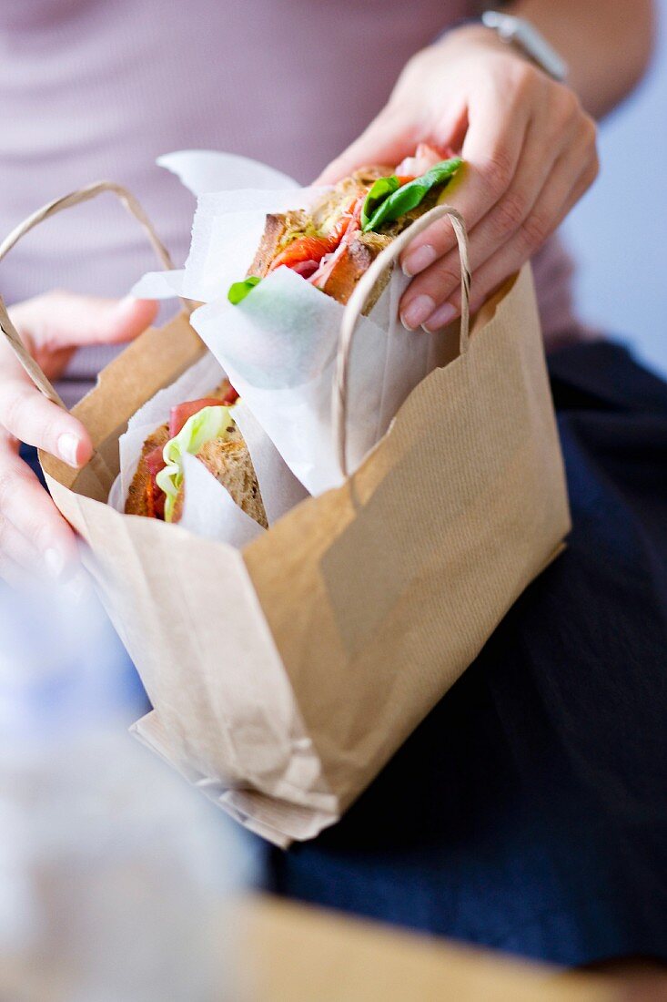 Frau packt Sandwich fürs Büro in eine braune Papiertüte