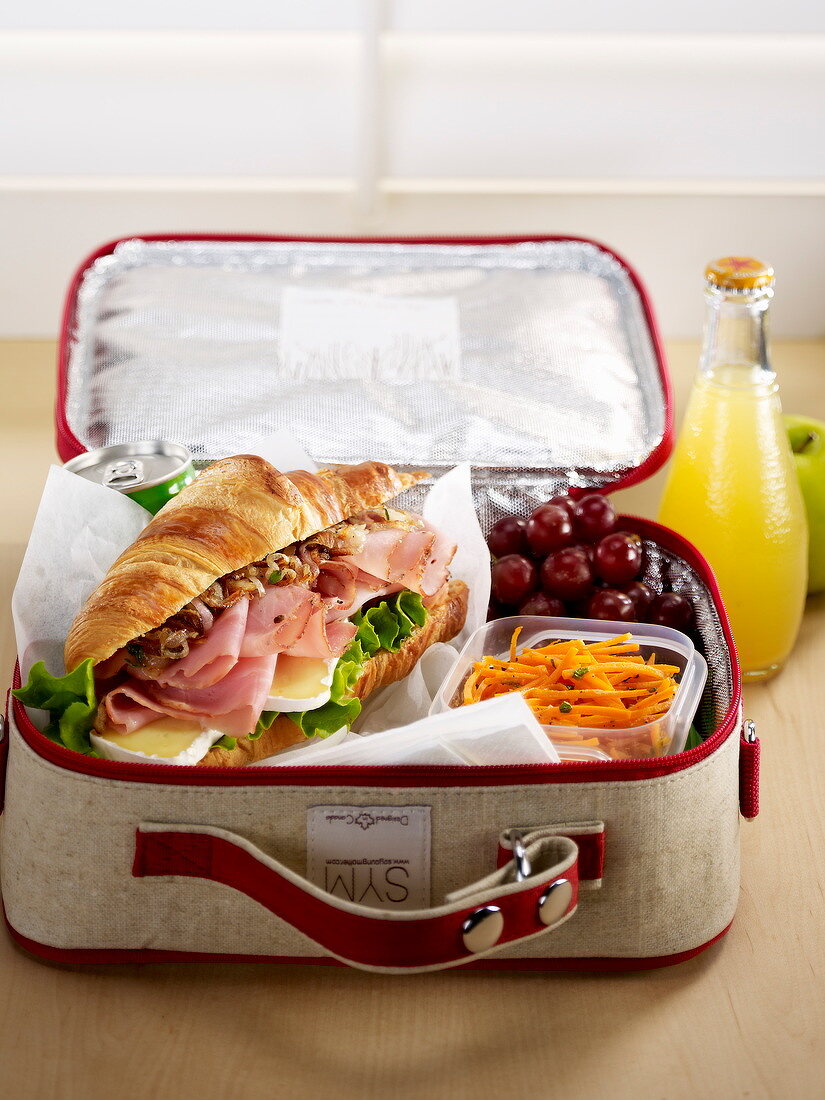 Croissant-Sandwich mit Möhrenrohkost und Trauben in Lunch-Koffer