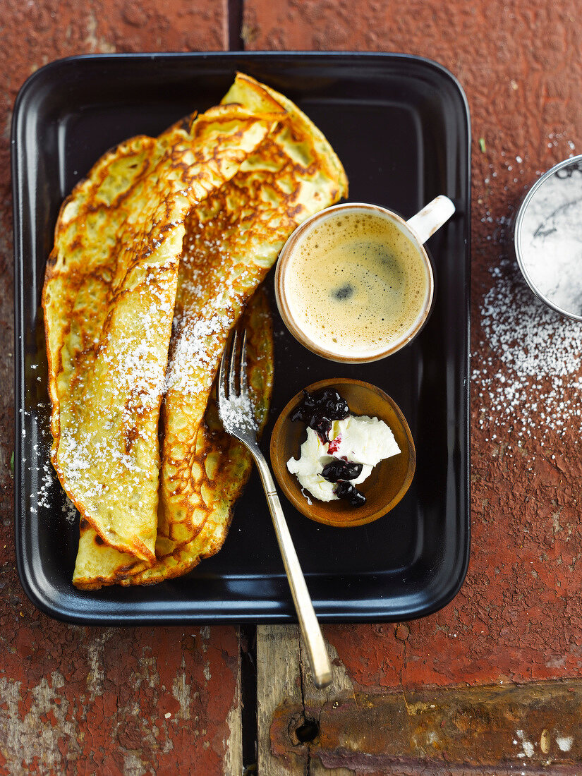 Pancake sprinkled with icing sugar,cup of coffee,bilberries and cream