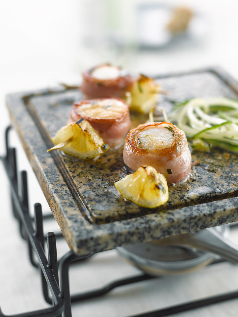 Scallops wrapped in bacon and sliced zucchinis on a cooking stone