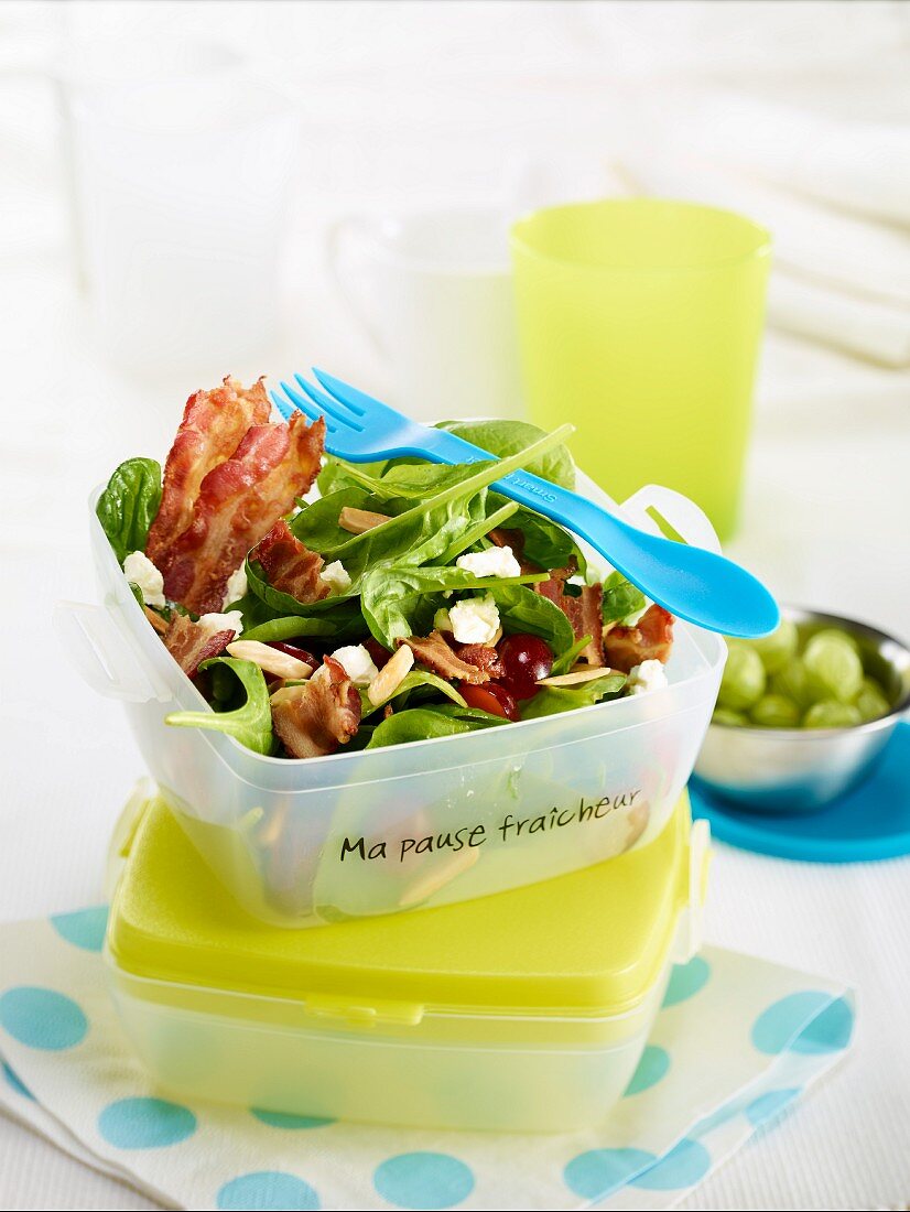 Spinatsalat mit Bauchspeck, Fetakäse und Kirschen in einem Platikbehälter