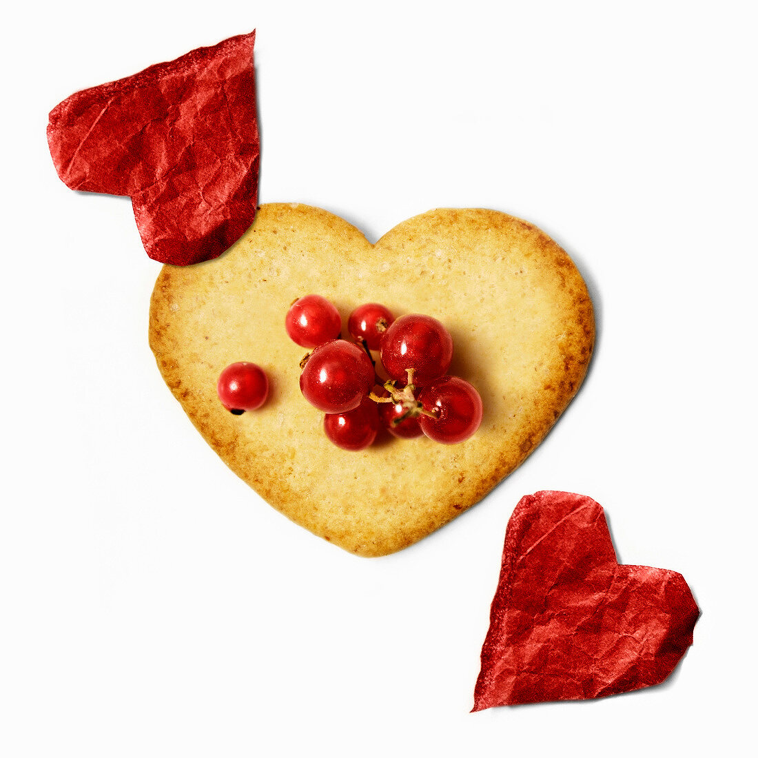Heart-shaped biscuit with redcurrants and red paper hearts