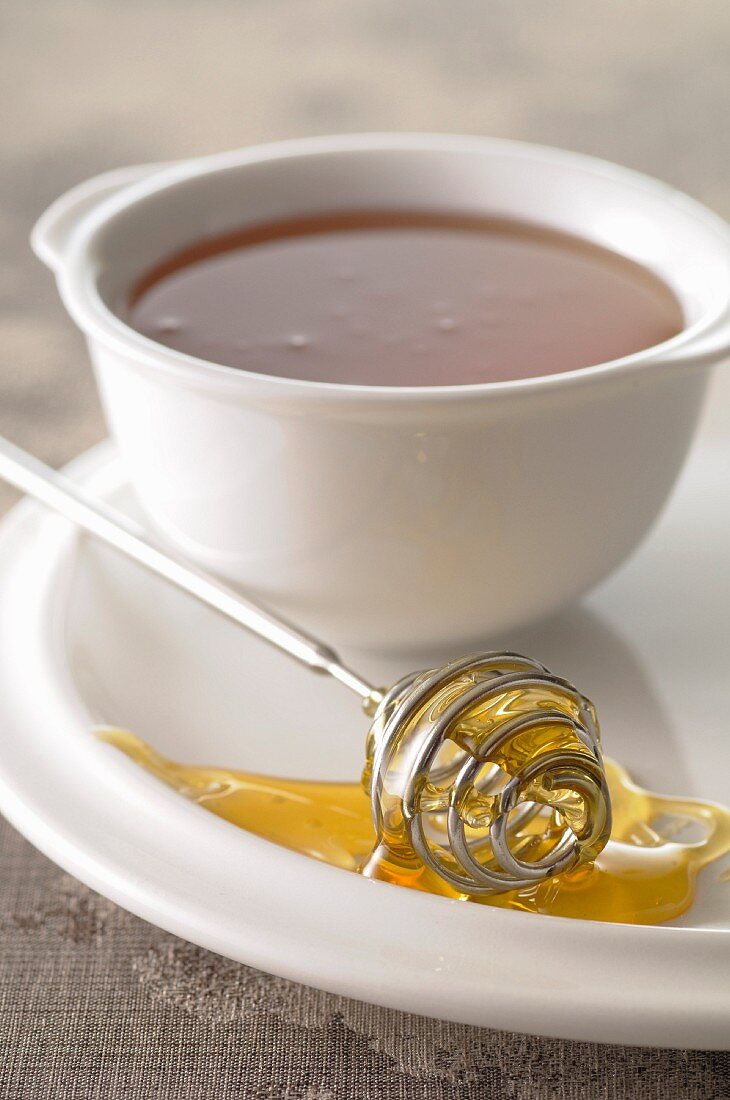 Honey spoon covered in honey and a bowl of honey