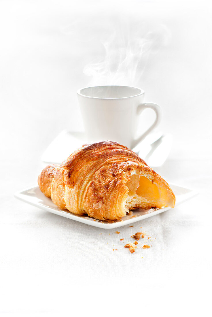 Angebissenes Croissant mit Tasse Kaffee