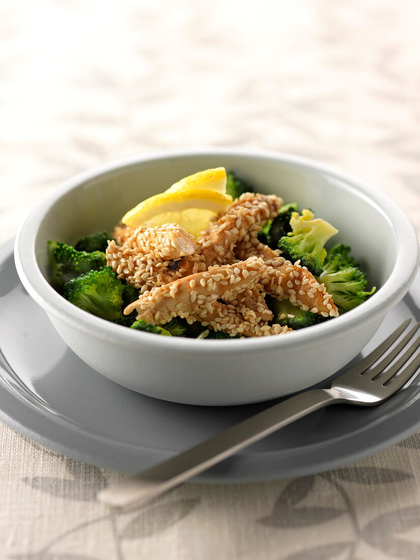 Sliced chicken breasts coated in sesame seeds with broccolis and lemon