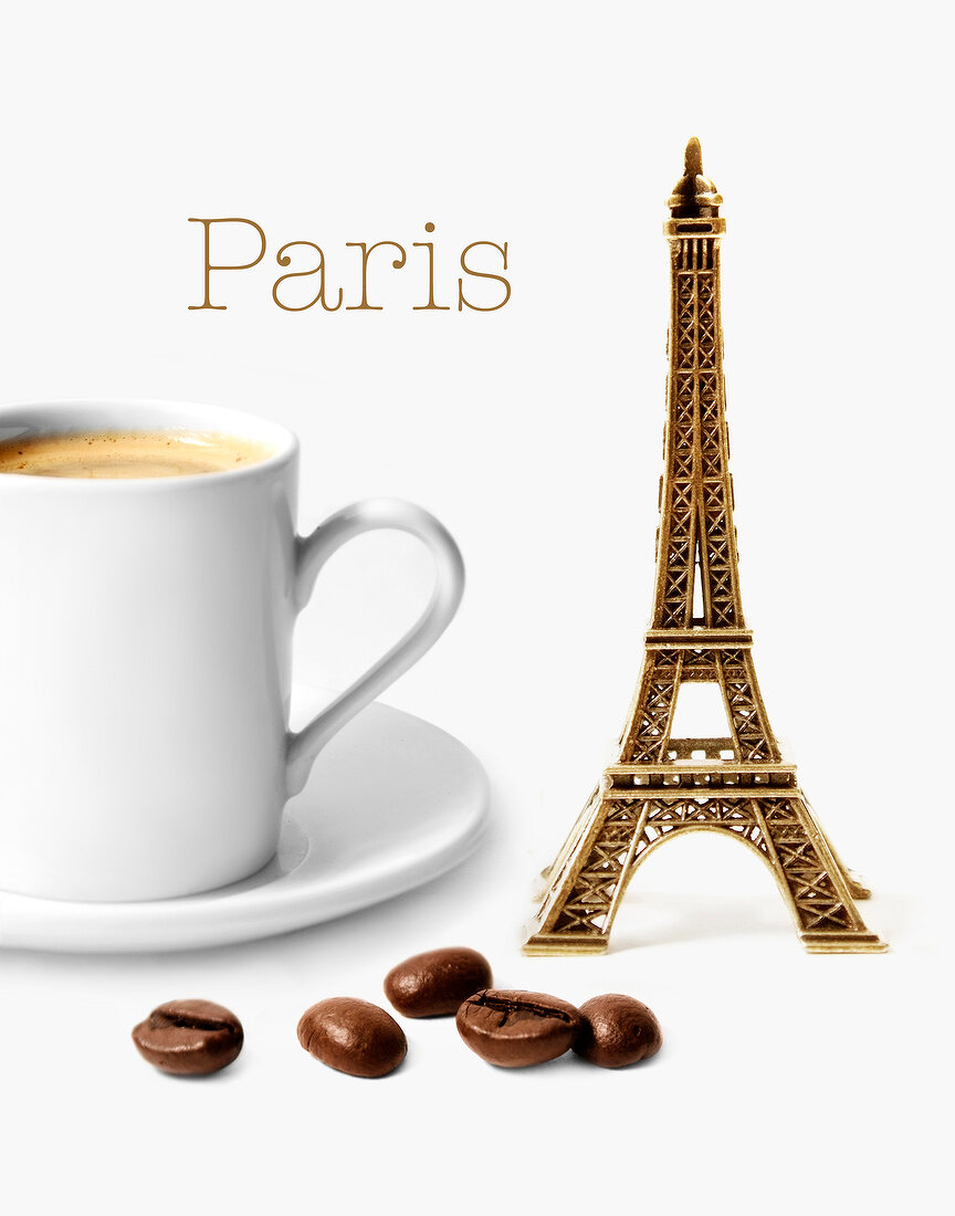 Komposition mit Mini-Eiffelturm, Tasse Kaffee und Kaffeebohnen vor weißem Hintergrund