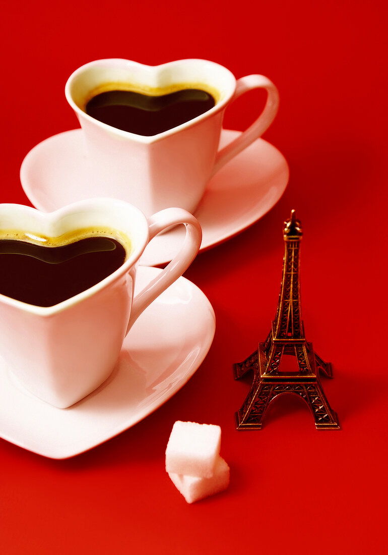 Komposition mit Mini-Eiffelturm und zwei herzförmigen Tassen Kaffee