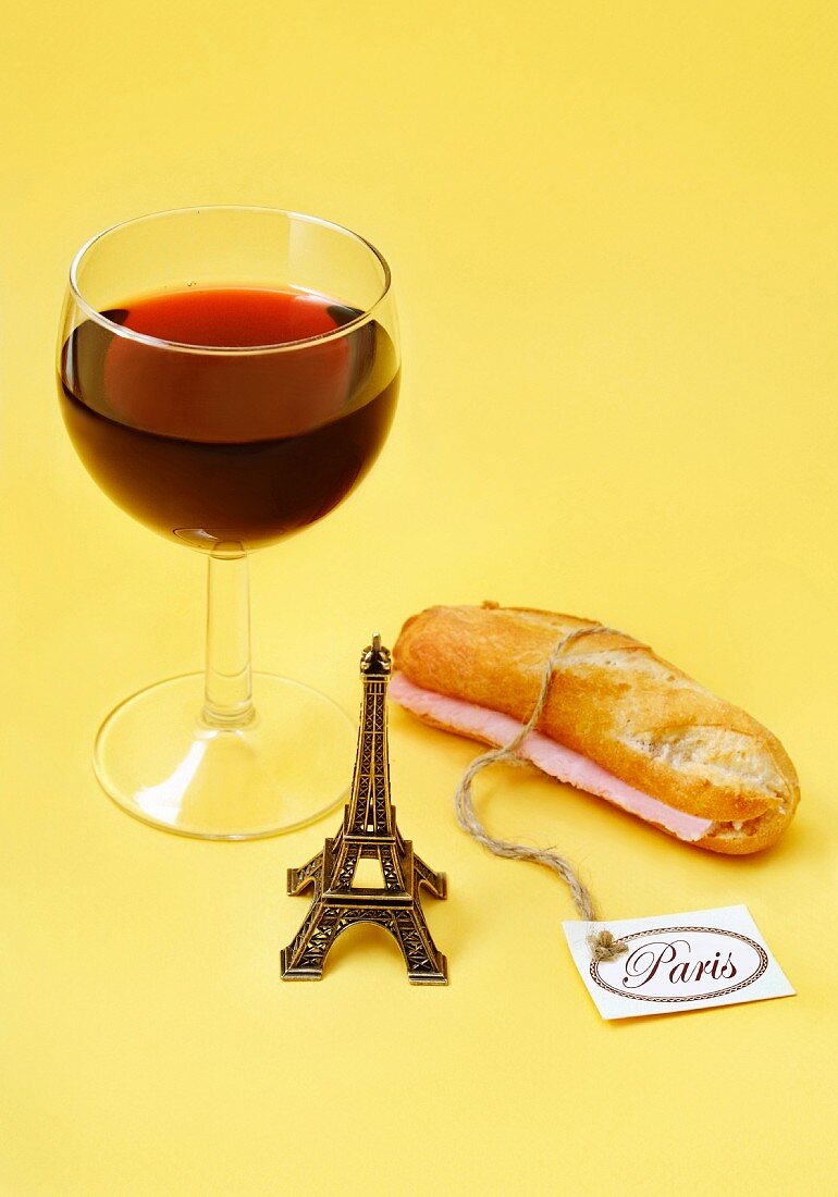 Stillleben mit einem Glas Rotwein, Schinkenbaguette und kleinem Eiffelturm (Paris)