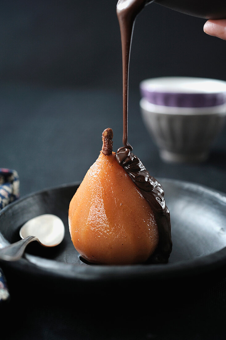 Pouring melted chocolate over a poached pear