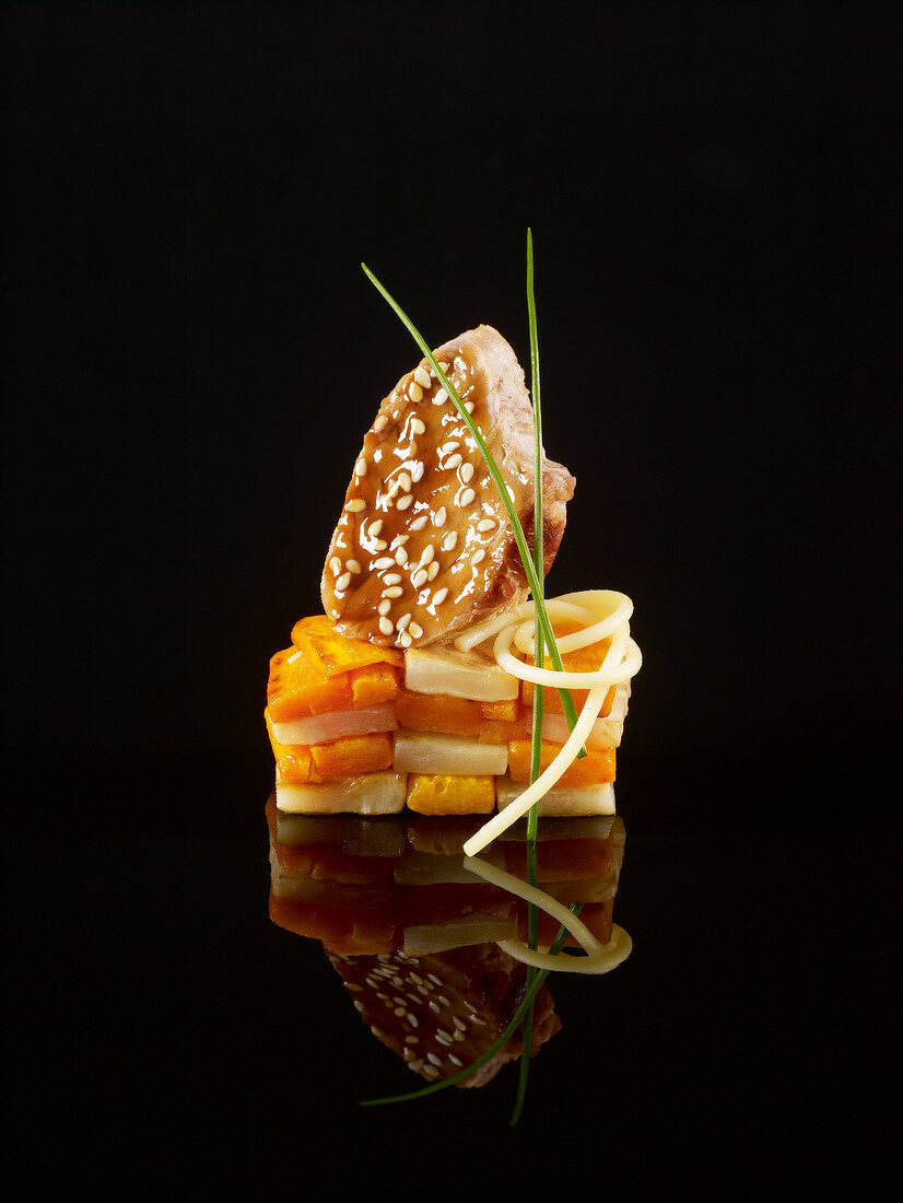 Soft carrot,glazed pork and sesame seed construction on a black background
