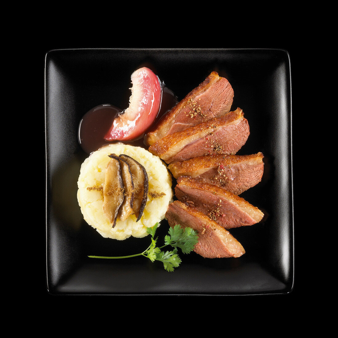 Entenbrust mit weisser Pfirsichsauce, Kartoffelpüree und Pilzen auf schwarzem Teller