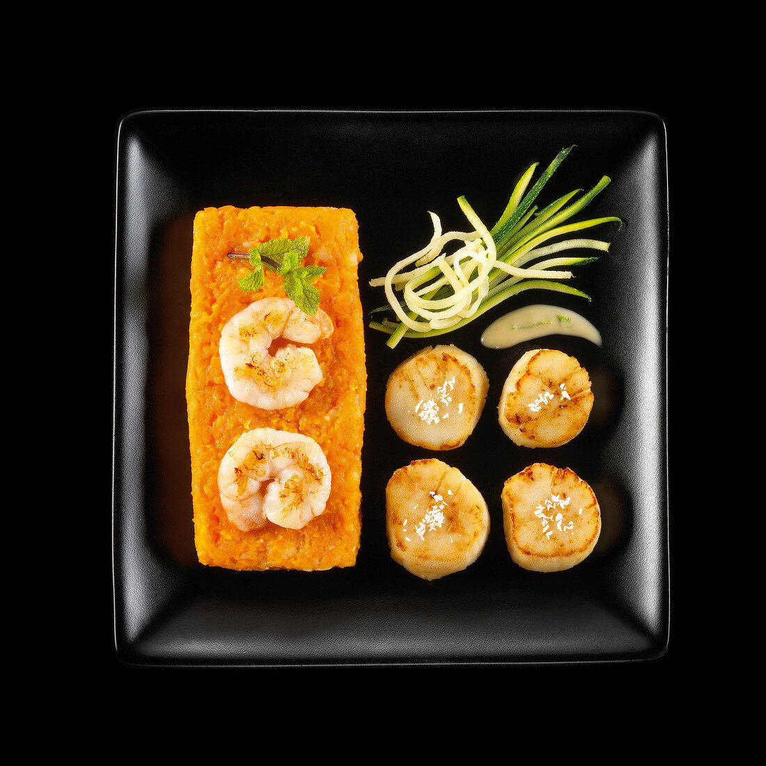 Roasted scallops,carrot mash with king prawns on a black background