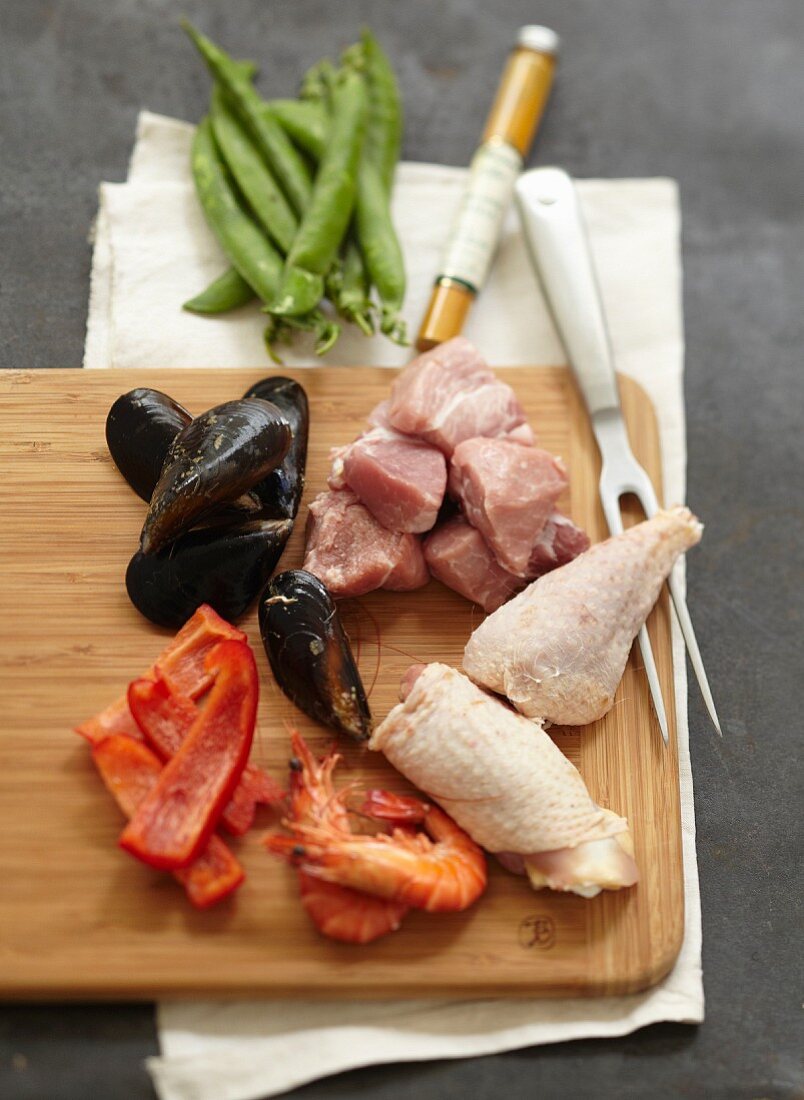 Holzbrett mit Zutaten für Paella (Muscheln, Paprika, Garnelen, Hähnchen und Kaninchenfleisch)