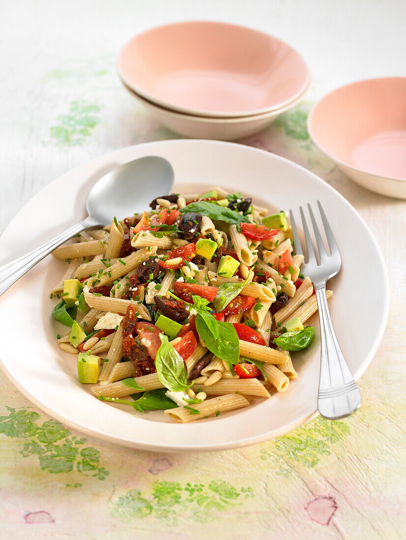 Pasta salad with fresh and dried tomatoes, avocado and basil