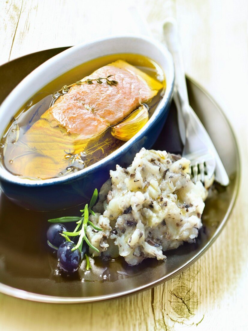 Piece of salmon marinating in olive oil, mashed potatoes with black olives