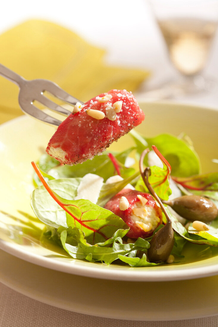 Salat aus Rote-Bete-Blättern, Kapern und Pinienkernen und rohe Rindfleischröllchen mit Frischkäse
