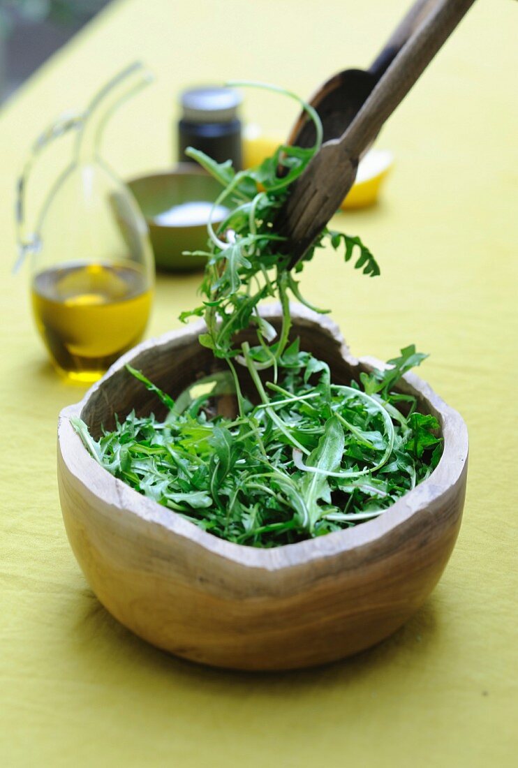Rucola-Löwenzahnsalat in einer Salatschüssel mit Salatbesteck und Dressing-Zutaten
