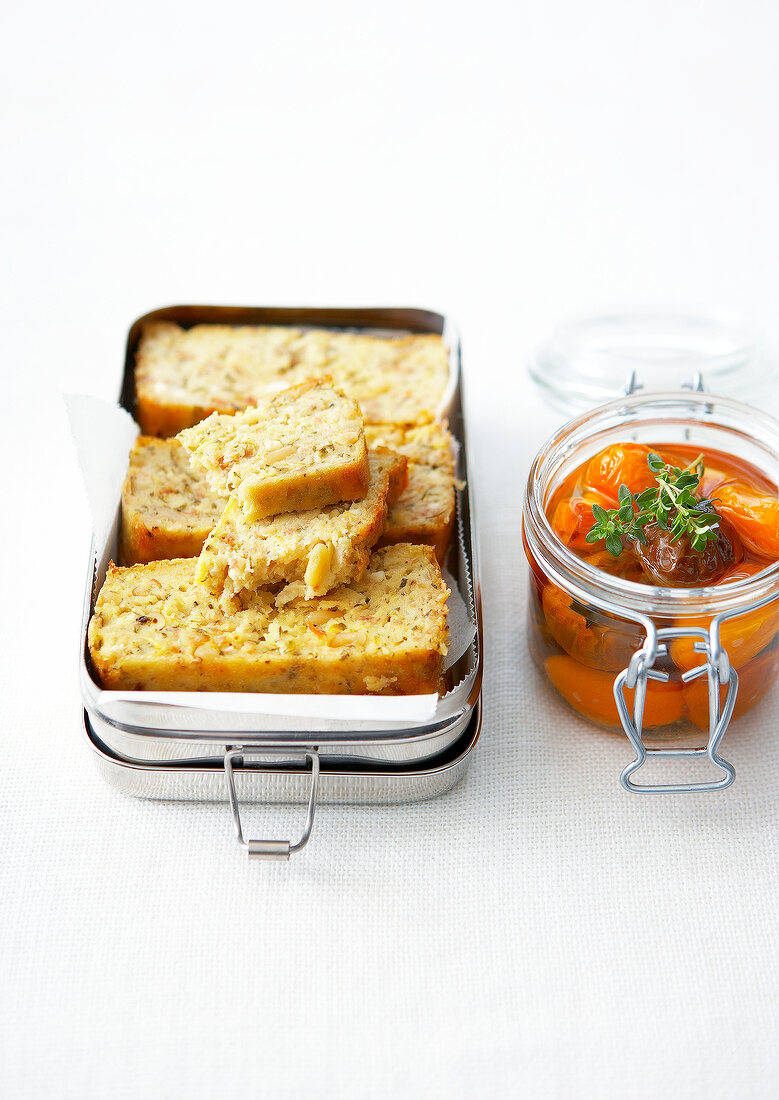 Lunch box full of sliced carrot and pine nut cake,jar of preserved tomatoes with fresh thyme