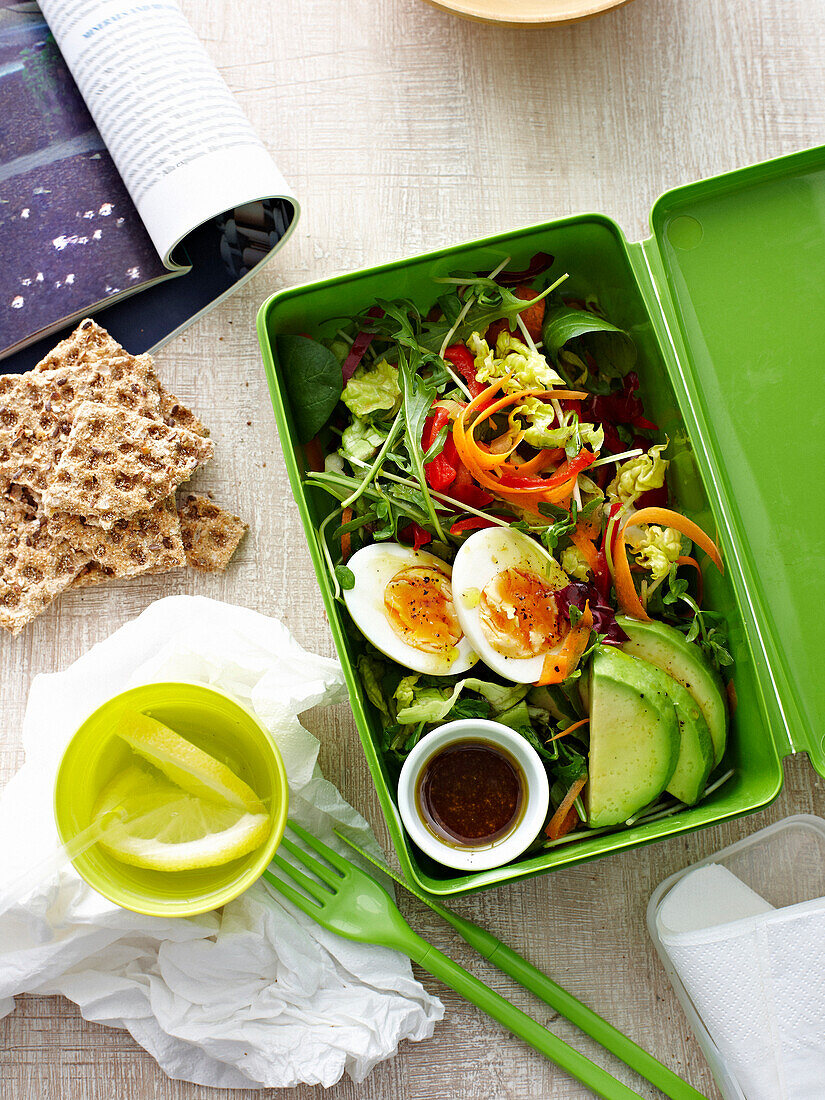 Blattsalat mit Avocado und gekochtem Ei in Lunchbox zum Mitnehmen