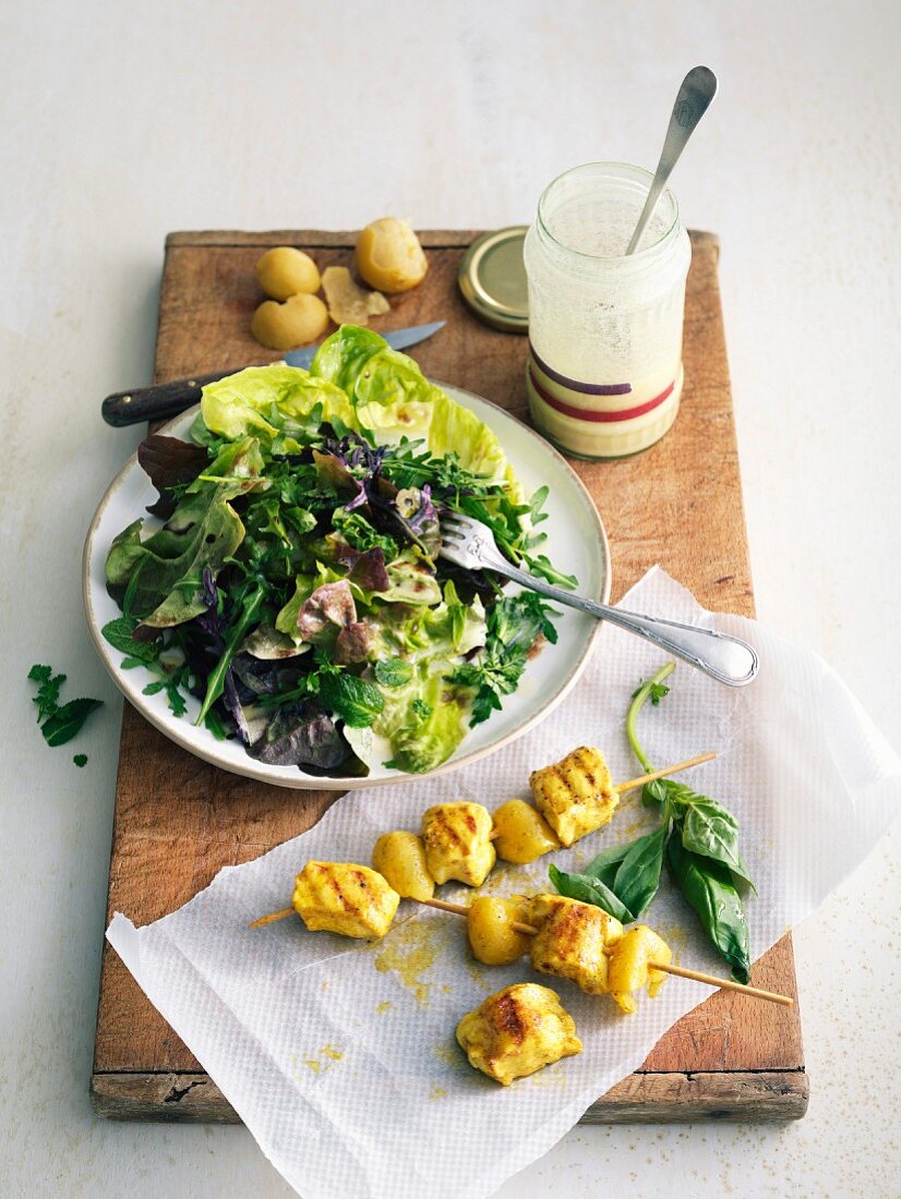 Mixed lettuce and fresh herb salad with white dressing, curried chicken-confit citrus skewers