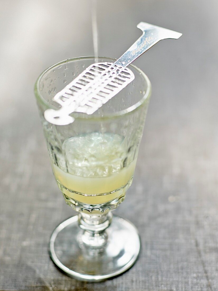Diluting a sugarlump on a spoon in th glass of Absinthe