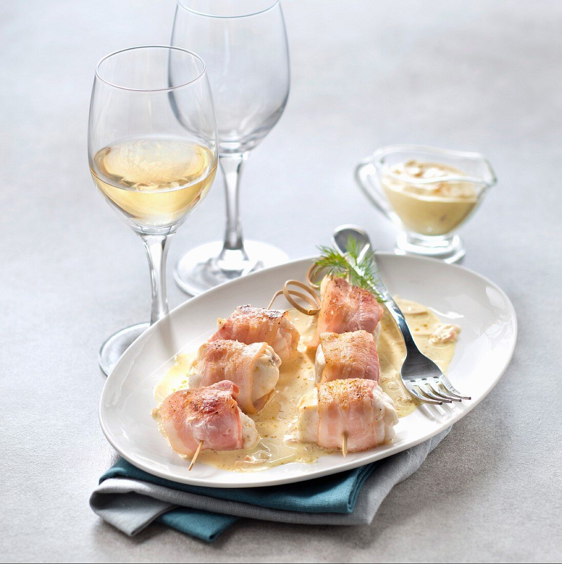 Fish skewer with smoked bacon and curry sauce, glass of white wine