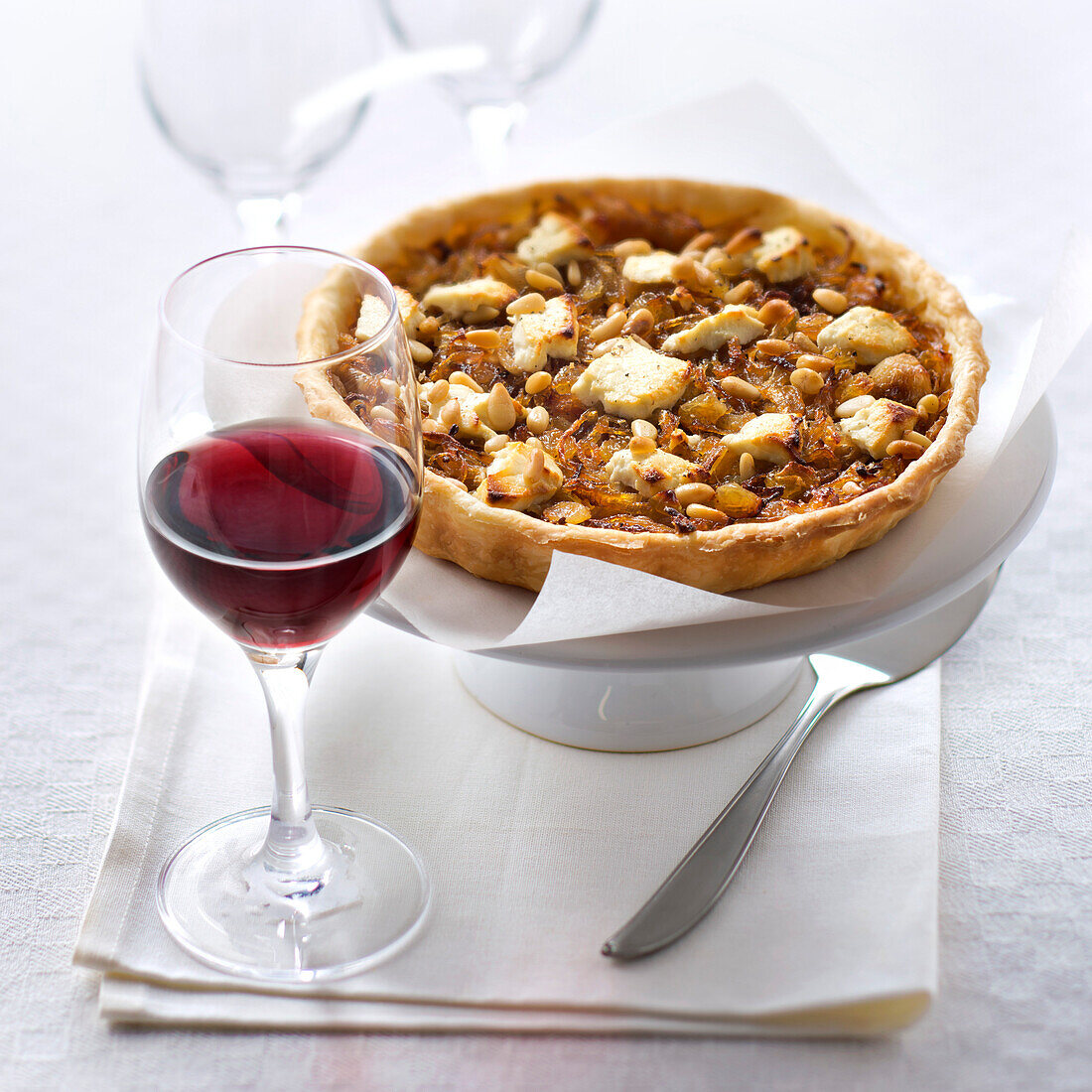 Tart with onion confit, pine nuts and goat cheese, served with a glass of red wine