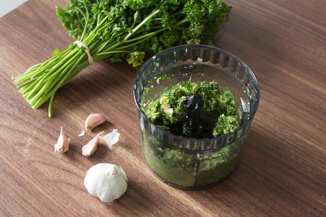 Garlic, parsley and butter being chopped in a vegetable hacker