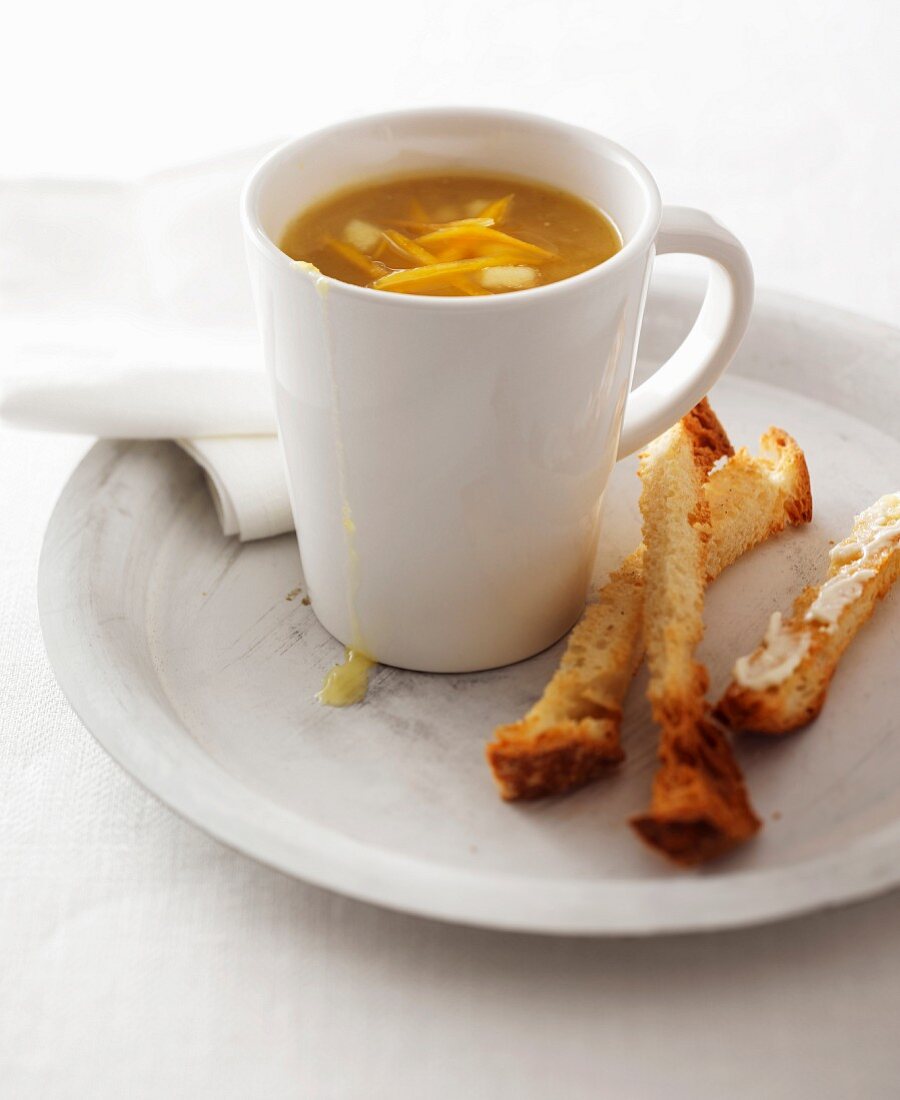 Kürbissuppe in der Tasse und Brotstangen mit Butter