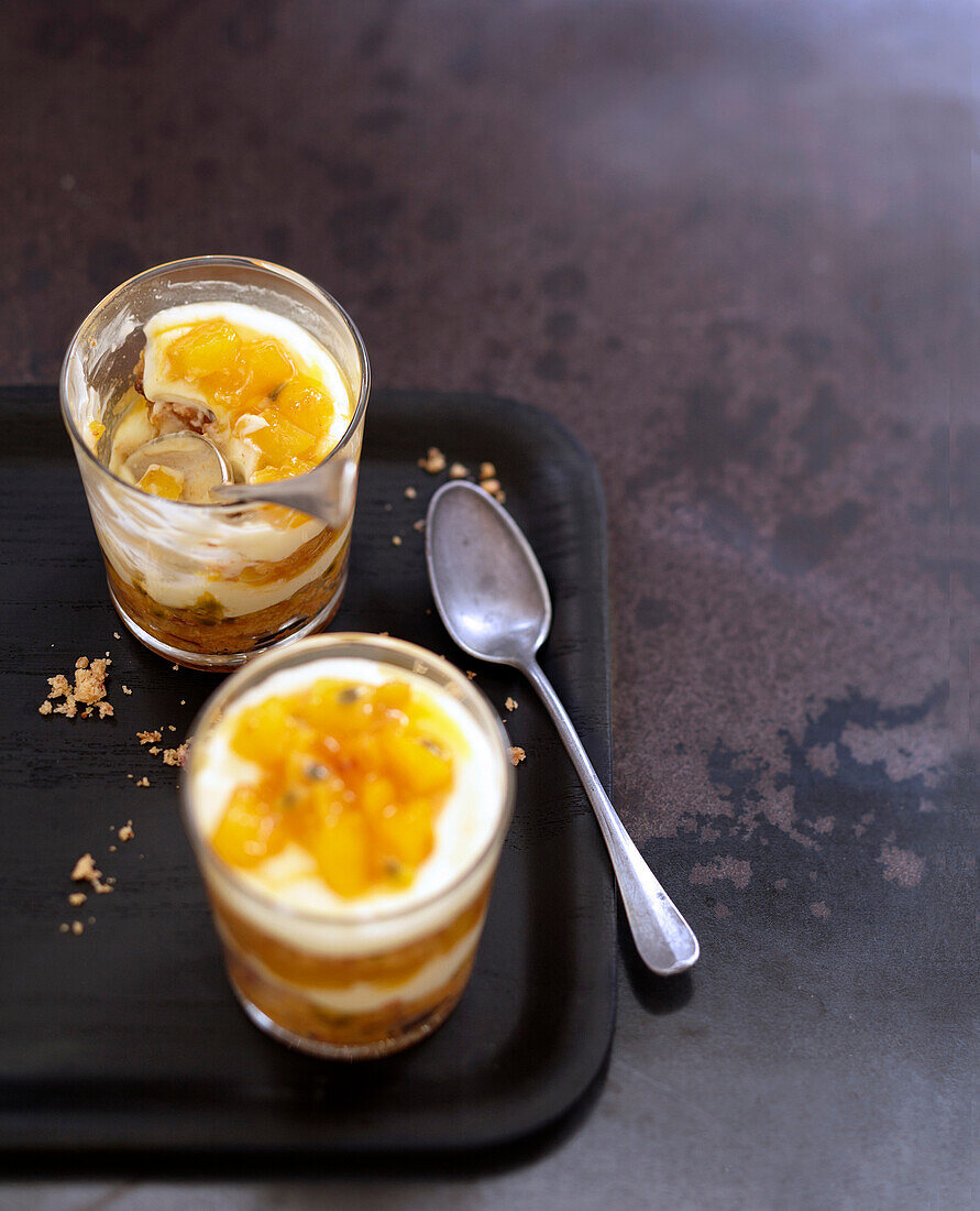 Schichtdessert mit karamellisierter Mango, Butterkuchenkrümel und Passionsfruchtsauce in Gläsern