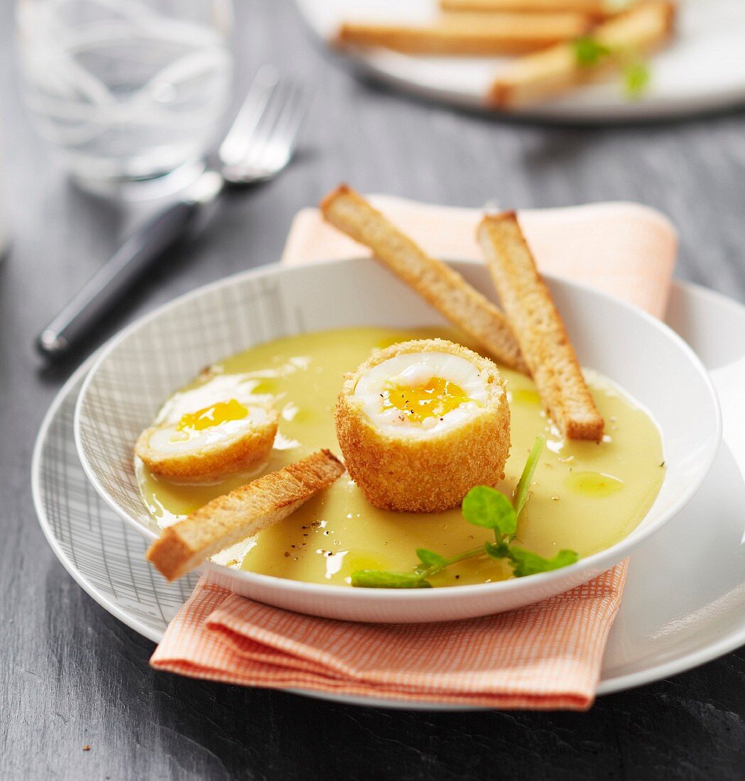 Soft-boiled egg coated in breadcrumbs with potato and cheese cream and bread fingers