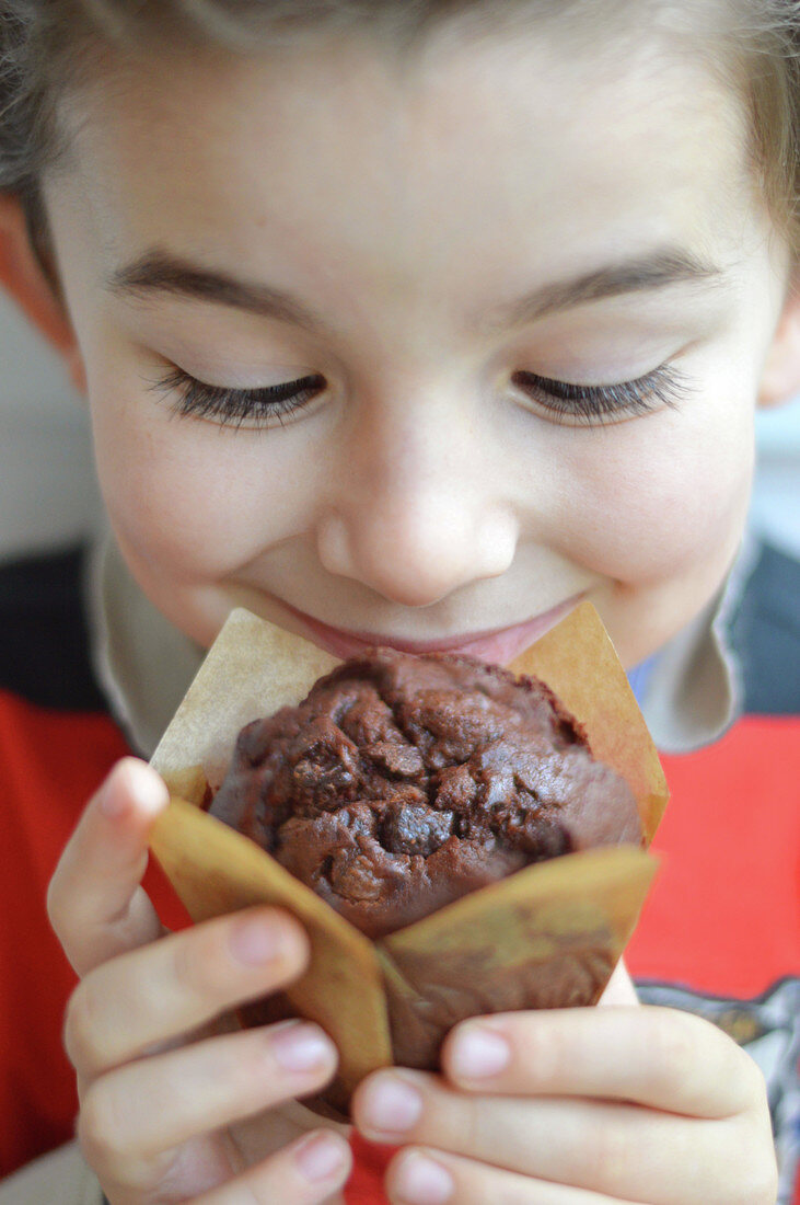 Junge schnuppert an einem Schokoladenmuffin