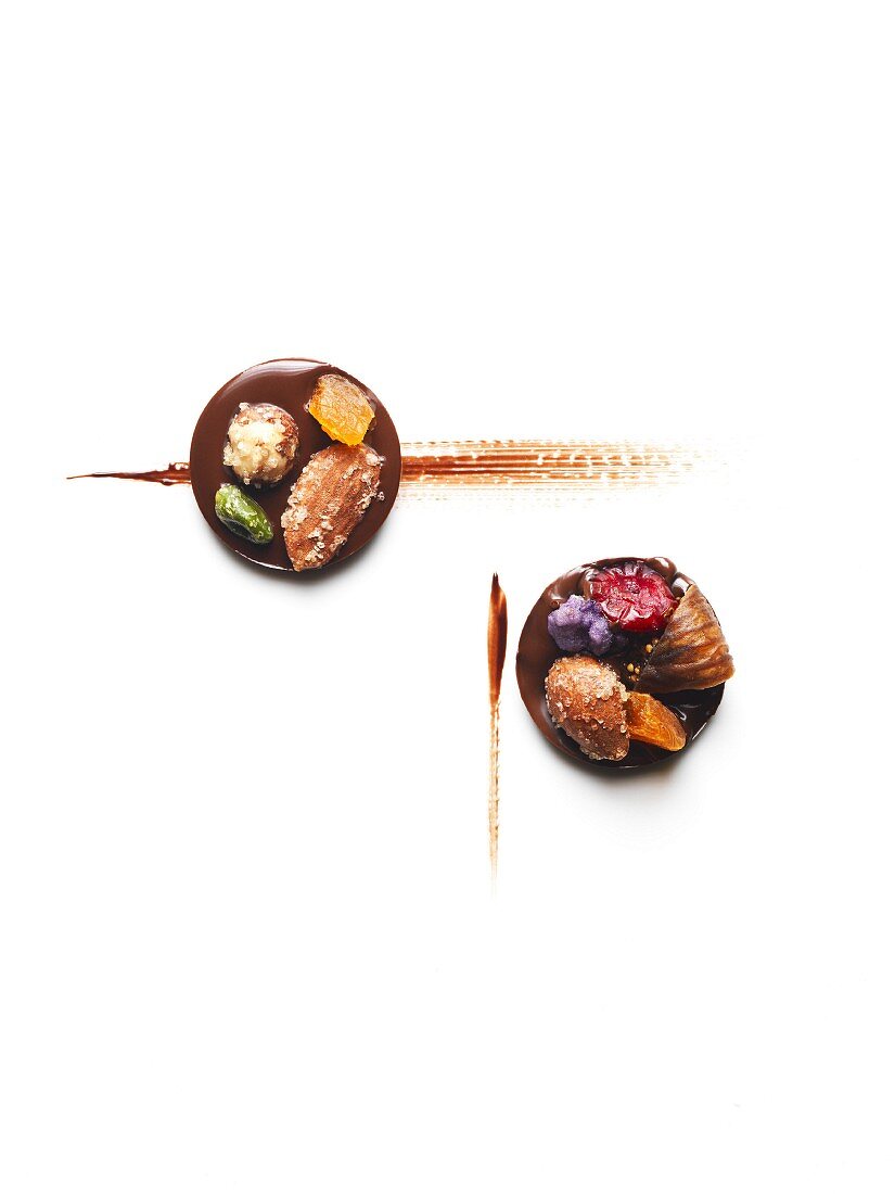Mendiants au chocolat (Schokoladentaler) mit Trockenfrüchten vor weißem Hintergrund