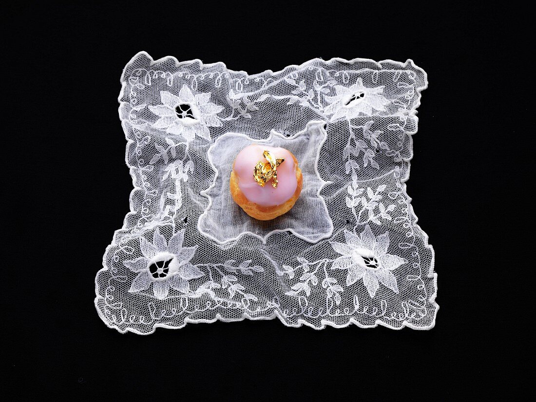 Small pink cream puff decorated with a golden leaf on a lace cloth