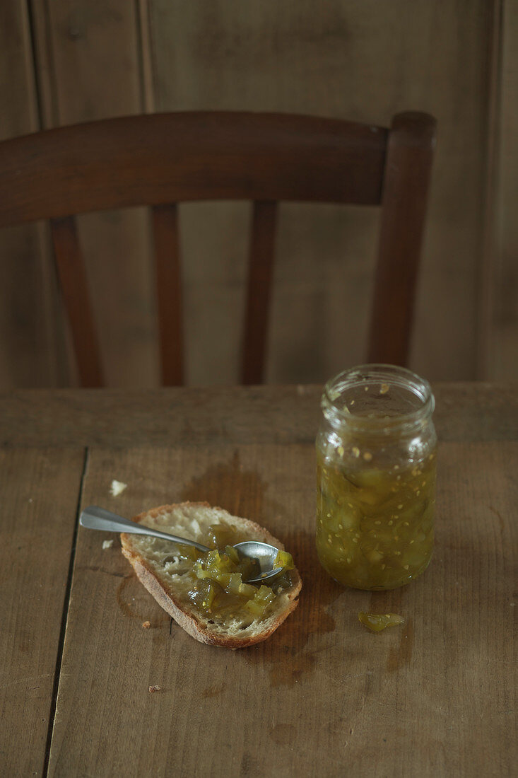 Jar of green tomato jam and spread on a slice of bread