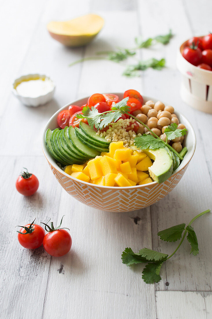 Orientalische Buddha Bowl mit Kirschtomaten, Mango, Kichererbsen, Avocado, Grieß und Gurke